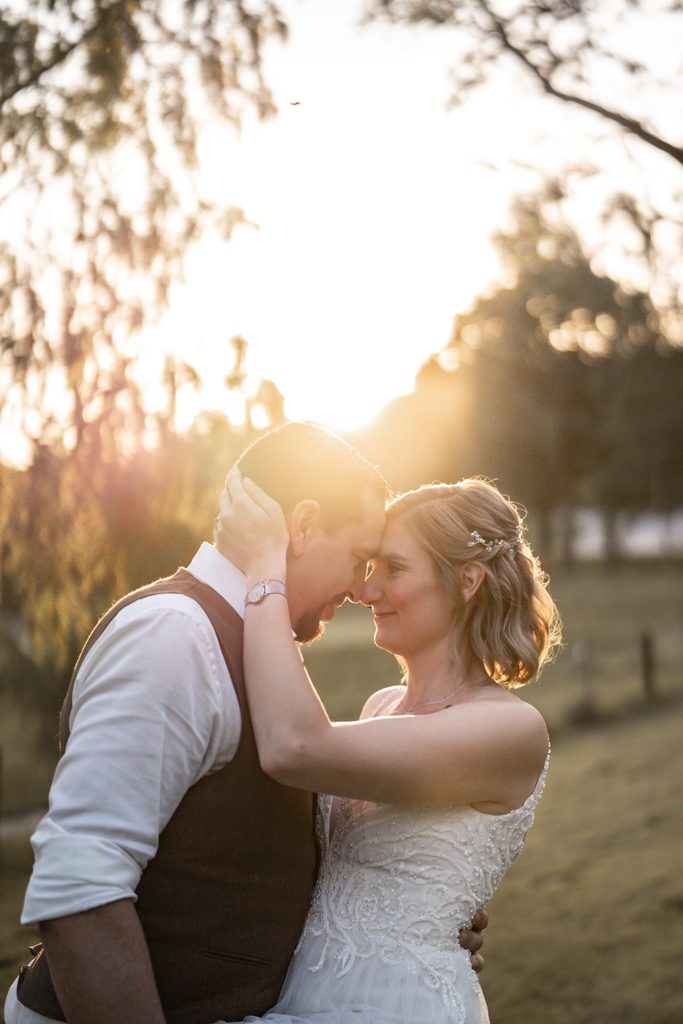 Hochzeitspaar schaut sich verliebt an. Im Hintergrund geht die Sonne unter