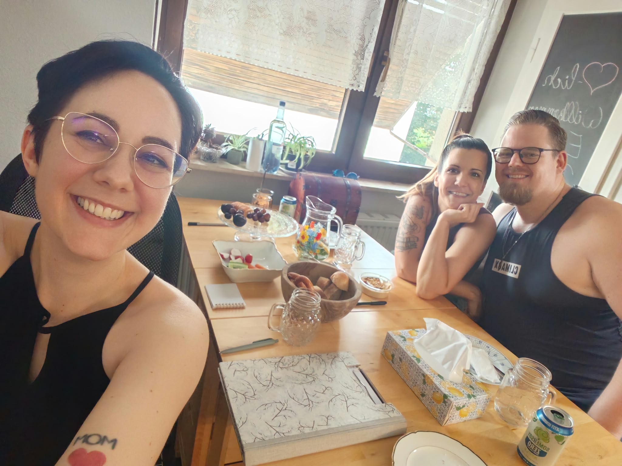 Traurednerin Jasmin sitzt mit Hochzeitspaar am Tisch und macht ein Seflie
